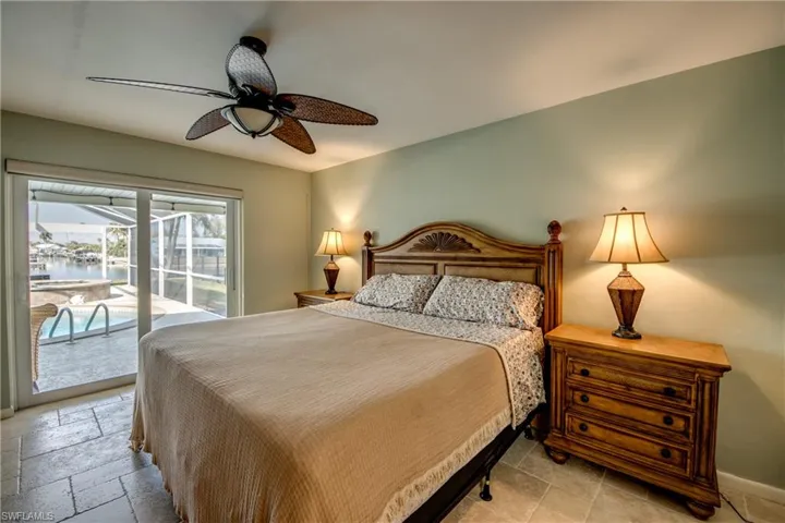 Bedroom with access to outside, a ceiling fan, stone tile floors, and a water view