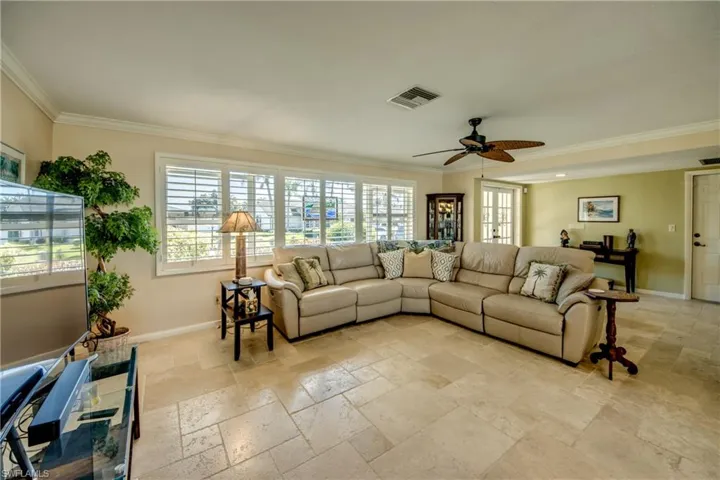 Living area with ceiling fan, stone tile floors, and crown molding