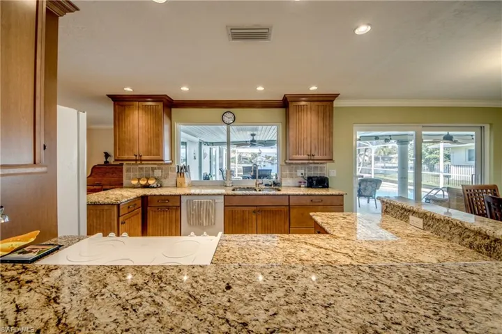 Kitchen with light stone countertops, wood finish cabinetry, recessed lighting, a ceiling fan, and white appliances