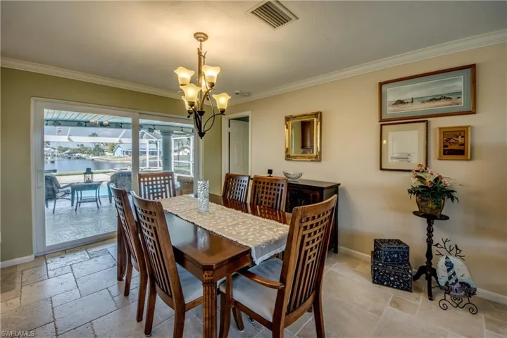 Dining room with stone tile floors, hanging lights, crown molding, and a water view