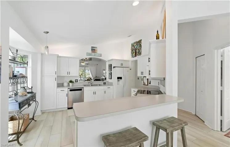Kitchen with white fridge with ice dispenser, a sink, vaulted ceiling, and stainless steel dishwasher