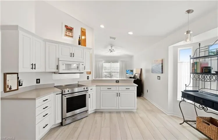 Kitchen featuring light countertops, a peninsula, white cabinets, white microwave, and stainless steel electric range oven