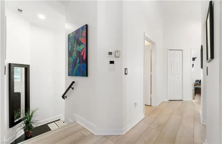 Hallway featuring baseboards, light wood-type flooring, visible vents, and a towering ceiling