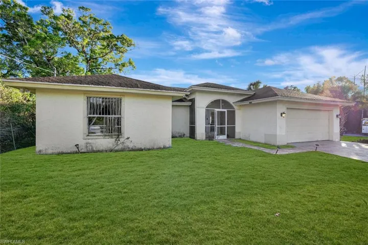 View of front facade with stucco siding, a front yard, concrete driveway, and an attached garage