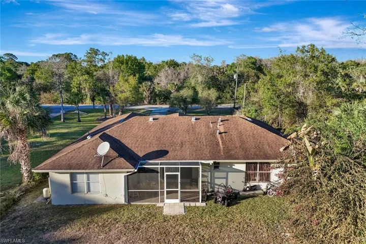 Rear view of house featuring a lawn, roof with shingles, stucco siding, and a sunroom