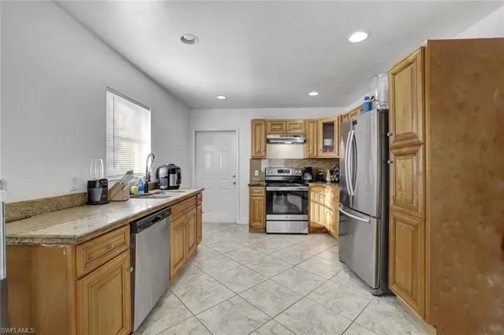 Kitchen featuring stainless steel appliances, wood finish cabinetry, glass fronted cabinets, light stone counters, and tasteful backsplash