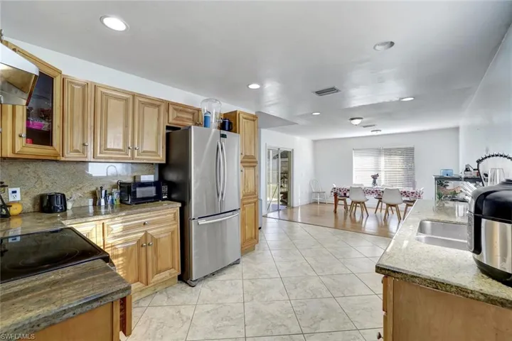 Kitchen with dark stone countertops, black appliances, glass insert cabinets, exhaust hood, and decorative backsplash