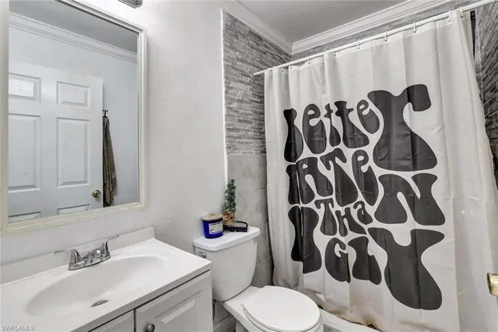 Full bathroom with a shower with curtain, vanity, crown molding, and tile walls