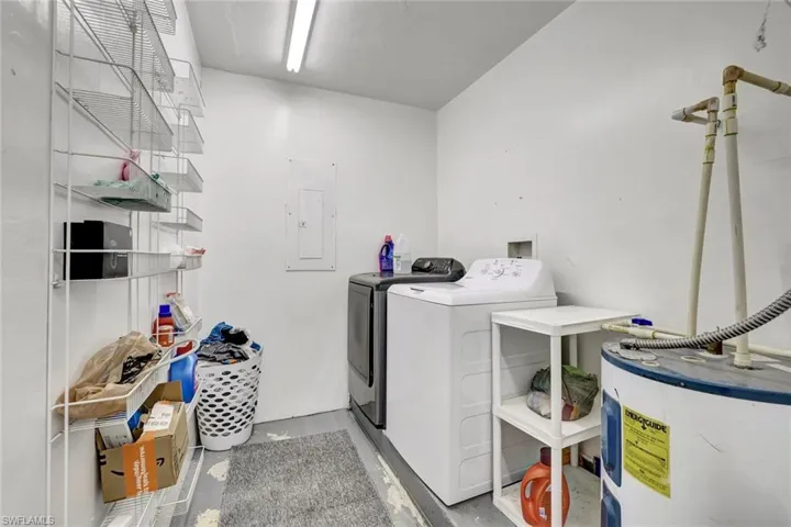 Laundry room with water heater, electric panel, washer and dryer, and concrete flooring