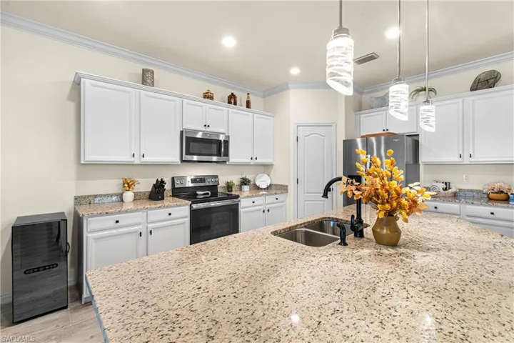 Kitchen with stainless steel appliances, hanging light fixtures, white cabinetry, crown molding, and light stone countertops