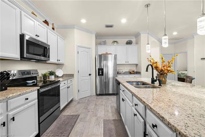 Kitchen featuring stainless steel appliances, pendant lighting, light stone counters, ornamental molding, and white cabinets