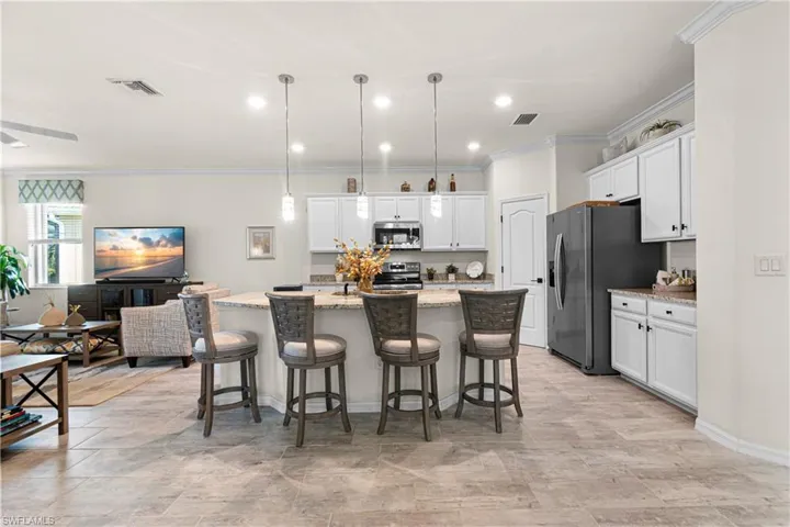Kitchen with pendant lighting, crown molding, an island with sink, appliances with stainless steel finishes, and light stone counters