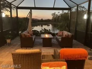 Patio terrace at dusk featuring an outdoor living space with a fire pit, glass enclosure, a sunroom, and a water view