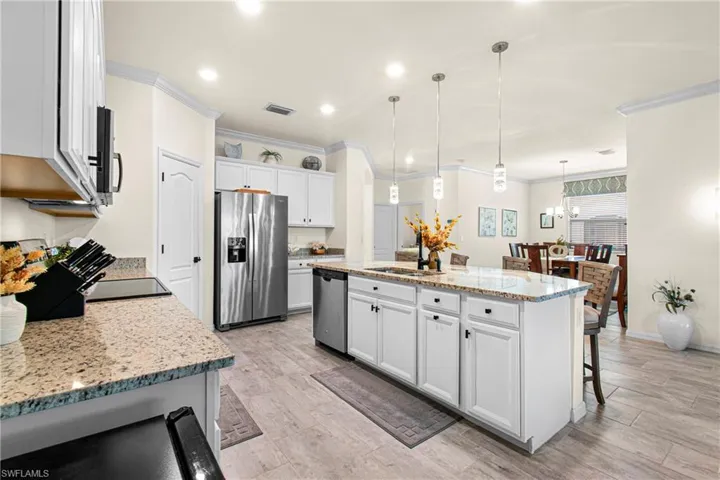 Kitchen featuring light stone counters, hanging light fixtures, stainless steel appliances, a kitchen bar, and a center island with sink