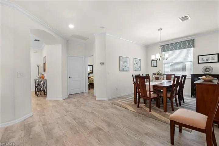 Dining room with ornamental molding, arched walkways, a chandelier, and light wood finished floors