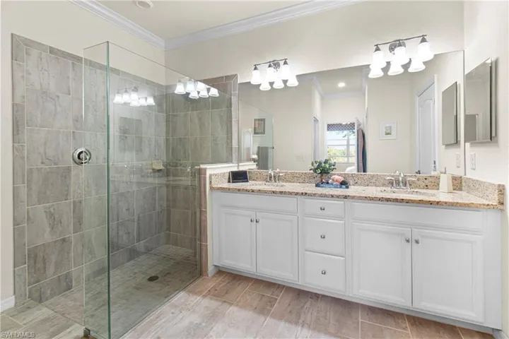 Main Bathroom featuring ornamental molding, double vanity, a walk in shower, and wood finish floors