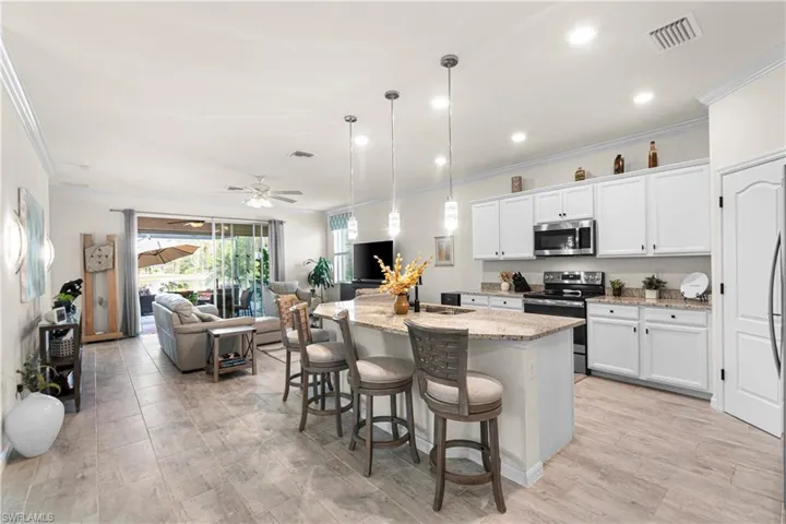Kitchen featuring hanging light fixtures, a kitchen island with sink, appliances with stainless steel finishes, white cabinetry, and crown molding