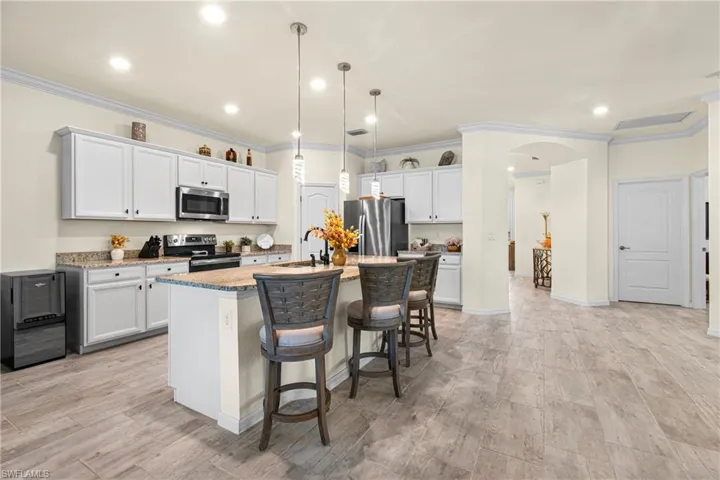 Kitchen featuring ornamental molding, arched walkways, white cabinets, a kitchen bar, and stainless steel appliances