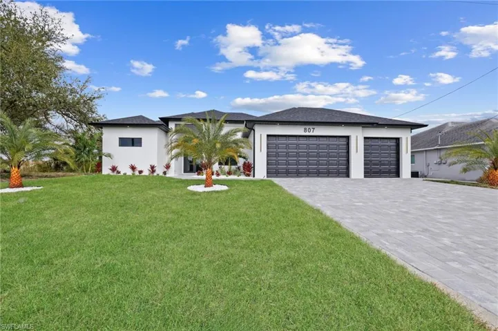 View of front of house featuring a garage, a front lawn, decorative driveway, and stucco siding