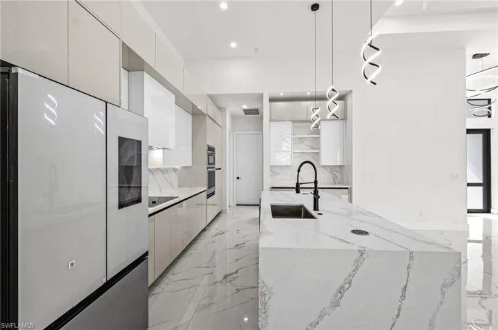 Kitchen with modern cabinets, marble finish floor, fridge, white cabinetry, and a sink
