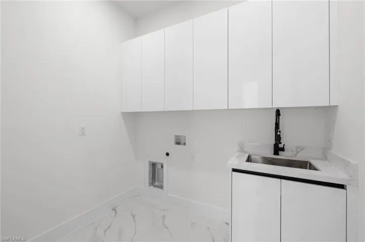 Clothes washing area featuring washer hookup, marble finish floor, cabinet space, a sink, and baseboards
