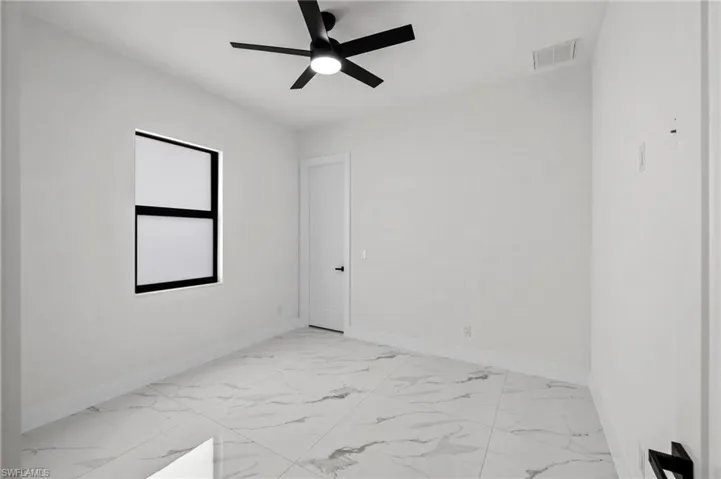 Spare room with ceiling fan, marble finish floor, visible vents, and baseboards