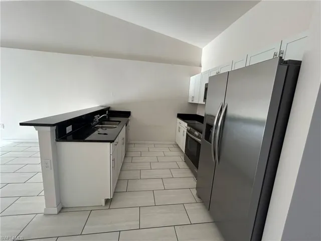 Kitchen featuring appliances with stainless steel finishes, dark countertops, vaulted ceiling, white cabinetry, and a peninsula
