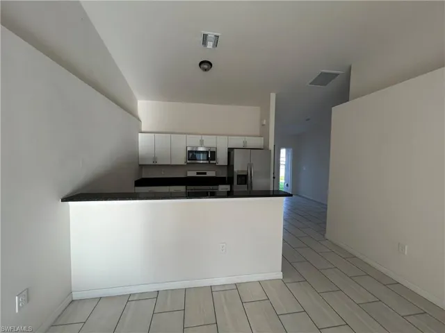 Kitchen featuring dark countertops, stainless steel appliances, white cabinets, a peninsula, and wood tiled floors