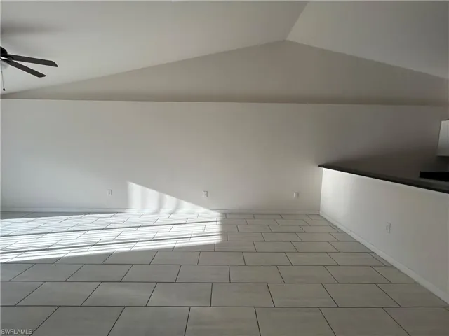 Unfurnished room with vaulted ceiling, ceiling fan, and light tile patterned floors