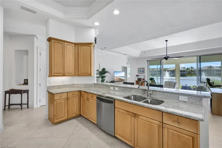 Kitchen with kitchen peninsula, light stone countertops, ornamental molding, sink, and dishwasher