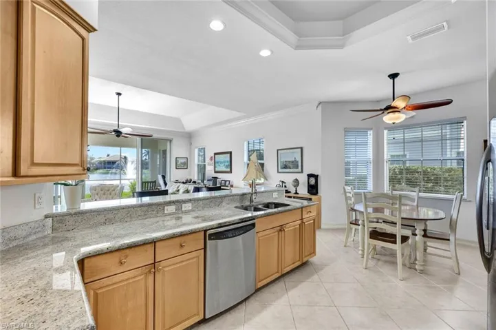 Kitchen featuring dishwasher, sink, a raised ceiling, light stone counters, and ornamental molding