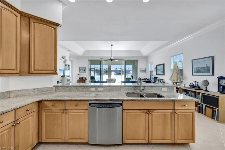 Kitchen with a tray ceiling, light stone countertops, sink, and stainless steel dishwasher