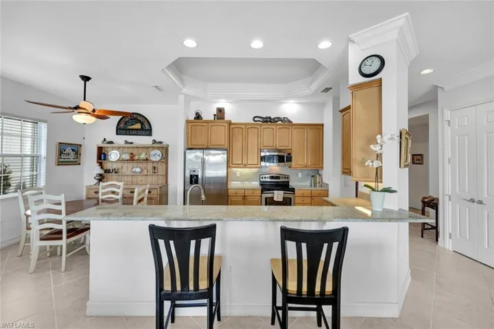 Kitchen with appliances with stainless steel finishes, backsplash, a kitchen breakfast bar, light stone counters, and ceiling fan