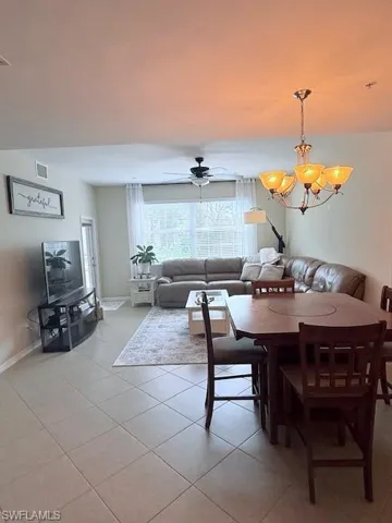 Dining room & living area with hanging lights, light tile patterned floors, and a ceiling fan.