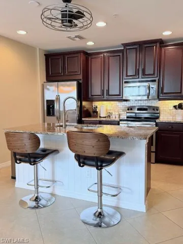 Kitchen with a breakfast bar, dark wood finish cabinets, stainless steel appliances, light stone counters, and recessed lighting.