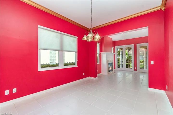 Spare room featuring crown molding, light tile patterned floors, a glass covered fireplace, and a chandelier