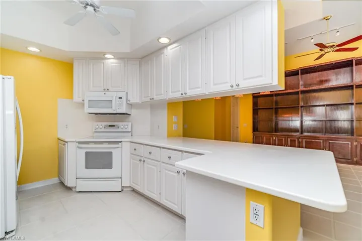 Kitchen featuring ceiling fan, white appliances, a peninsula, light countertops, and white cabinetry