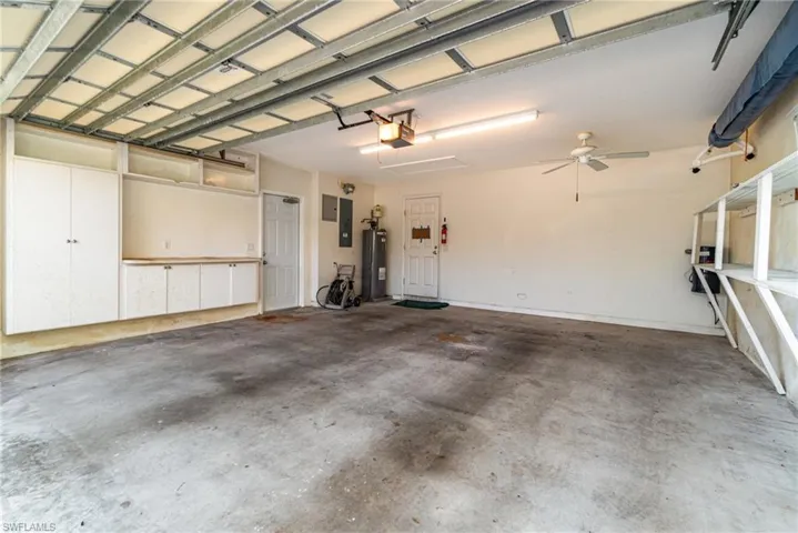 Garage with electric panel, water heater, a garage door opener, and a ceiling fan
