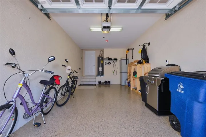 Garage featuring freestanding refrigerator, a garage door opener, electric water heater, and a textured wall