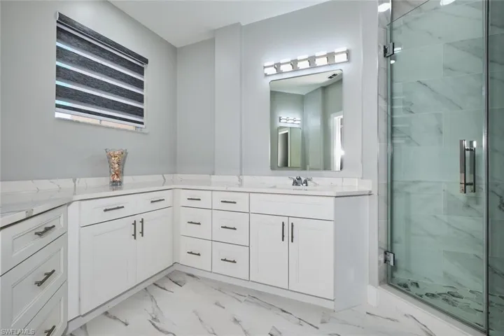 Bathroom featuring vanity, a marble finish shower, and light marble finish floors