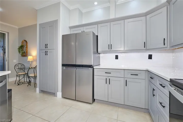 Kitchen featuring stainless steel appliances, crown molding, backsplash, light stone countertops, and gray cabinetry