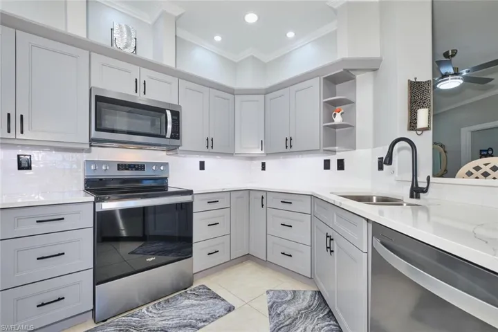 Kitchen with crown molding, stainless steel appliances, decorative backsplash, open shelves, and gray cabinets