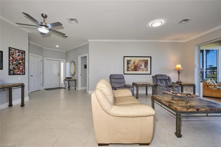 Living area with ornamental molding, light tile patterned floors, and a ceiling fan