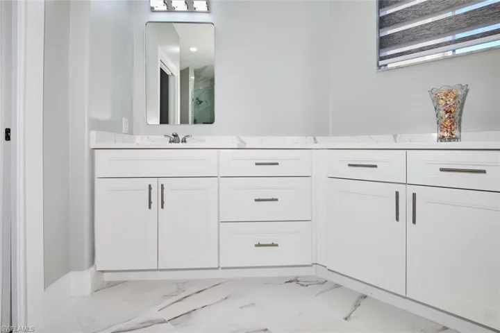Full bath featuring double vanity, light marble finish flooring, and a marble finish shower
