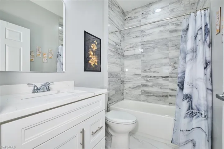 Full bath featuring shower / tub combo, vanity, and marble look tile flooring