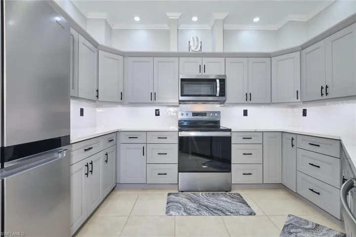 Kitchen with stainless steel appliances, tasteful backsplash, gray cabinets, light stone countertops, and crown molding