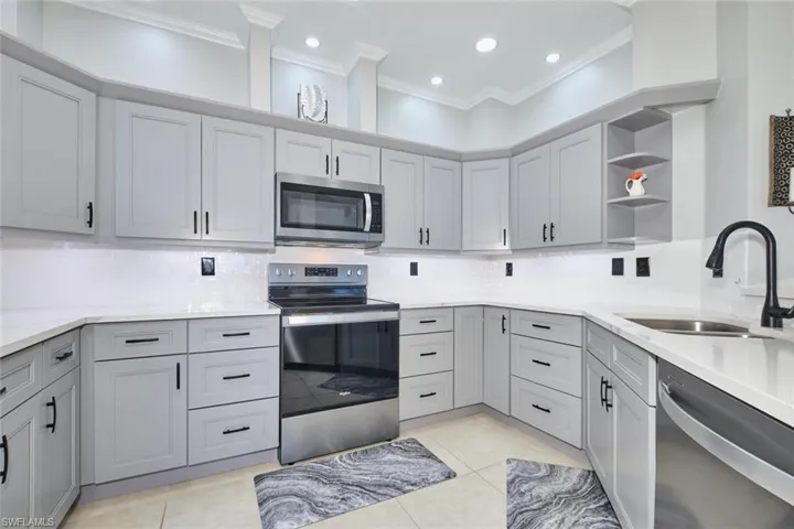 Kitchen featuring open shelves, stainless steel appliances, light stone counters, decorative backsplash, and gray cabinetry