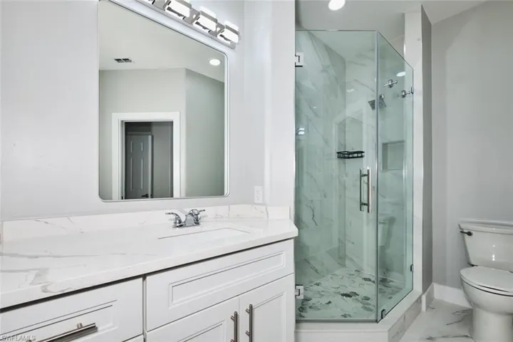 Bathroom featuring vanity, a marble finish shower, light marble finish floors, and recessed lighting