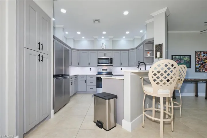 Kitchen with decorative backsplash, stainless steel appliances, light countertops, gray cabinetry, and a kitchen bar
