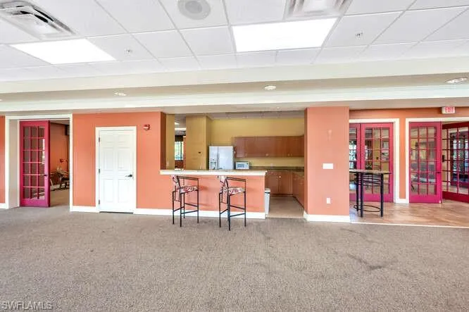 Kitchen featuring a drop ceiling, french doors, white refrigerator with ice dispenser, kitchen peninsula, and a breakfast bar area